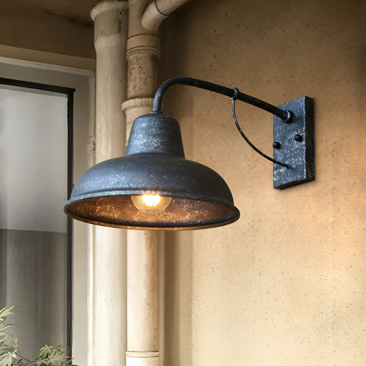 Wandlamp met gespikkelde donkere afwerking en brandende lamp tegen een beige muur naast een regenpijp en venster. 6