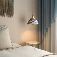 Brandende hanglamp met blauw bloemendecor boven een marmeren bijzettafel naast een bed met linnen kussens en blauwe gordijnen. 2