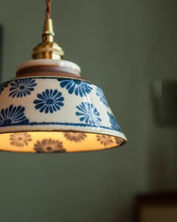 Close-up van de keramische kap met blauwe bloemen, glanzende glazuur, bruine rand en messing fitting aan getwijnd snoer. 6