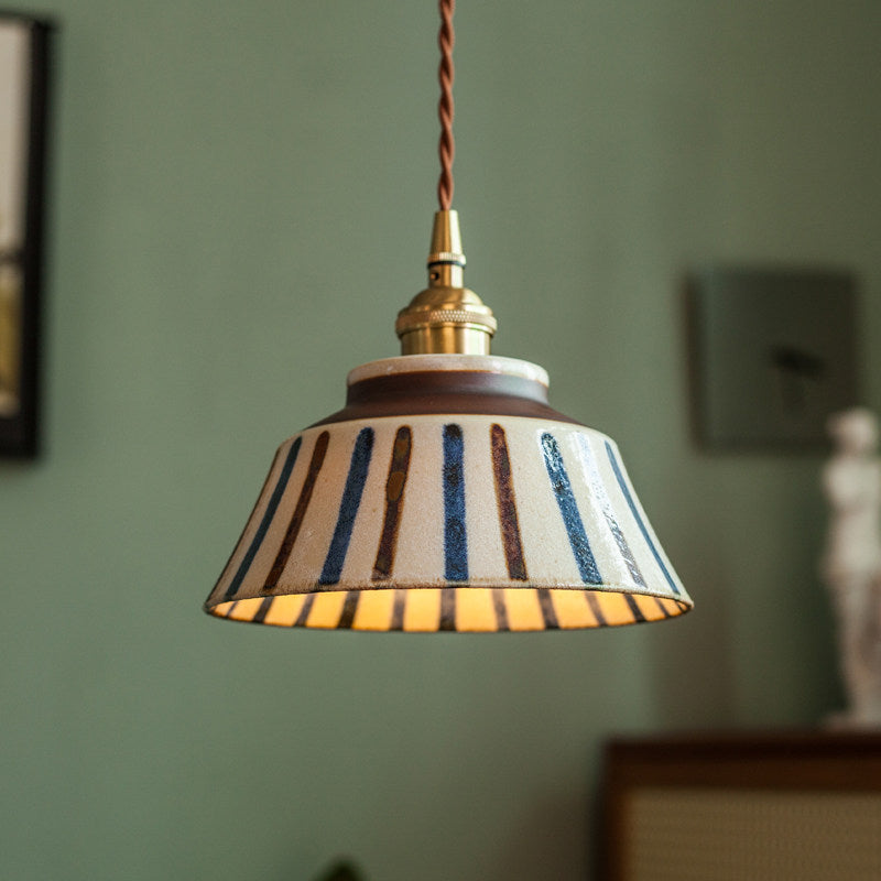 Hanglamp met verticale blauwe en bruine strepen op de keramische kap, van dichtbij voor een groene muur. 3