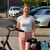 Lachende vrouw staat naast haar fiets met een hand op het zwarte zadel, een fietstas achter het zadel. 7
