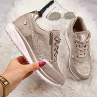 Hand houdt een taupe sneaker met zijrits vast, met de tweede schoen en een zonnebril op wit bont op de achtergrond. 7