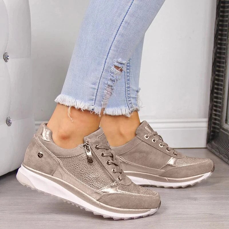 Taupe sneakers met ritssluiting aan de zijkant en glinsterende details, gedshowd door een model in gescheurde lichtblauwe spijkerbroek. 1