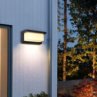 Wandlamp aan een lichte houten buitenwand met een regenpijp, met bomen in de avondschemering 6