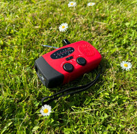 Rode handradio met draagkoord ligt in het gras tussen madeliefjes, gezien van boven 2