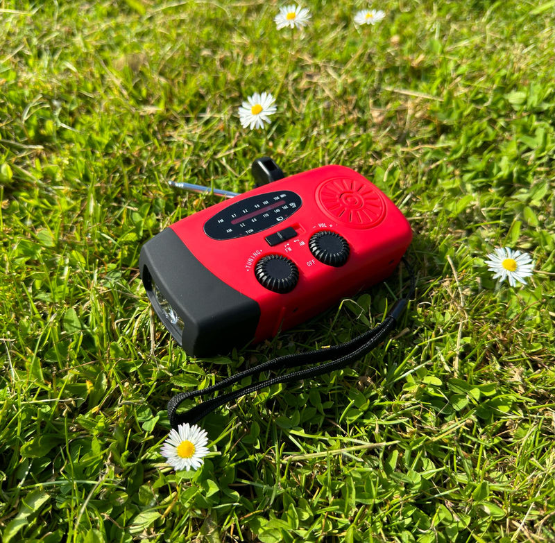 Rode radio met zwarte polsband en uitgeschoven antenne ligt in het gras tussen madeliefjes 2
