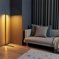 Verticale lamp met amberkleurig licht in een donkere woonkamer naast een grijze bank met kussens en een kleed 11