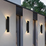 Drie zwarte wandlampen op een rij tussen ramen van een gevel, elk met warm licht dat omhoog en omlaag op de muur valt. 6