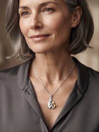 Vrouw met grijs bobkapsel in donkergrijze blouse draagt de ketting met zilverkleurige hanger en gouden kat. 10