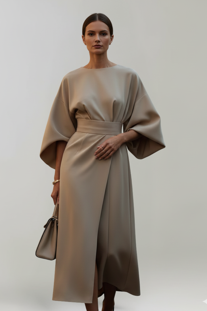 Model draagt de jurk in beige van voren, met een hand op de taille 6