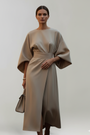 Model draagt de jurk in beige van voren, met een hand op de taille 6