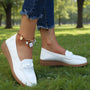 Witte loafers met gevlochten detail en bruine zool gedragen in een park, met een spijkerbroek met rafelrand. 5