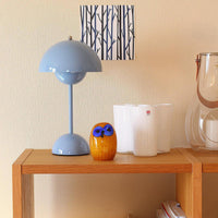 Lichtblauwe lamp op een houten rek naast een oranje glazen uil en witte vazen 31
