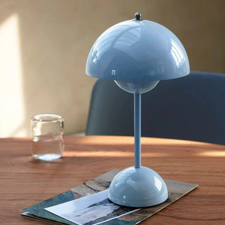 Glanzend lichtblauwe tafellamp op een houten tafel naast een glas water en een tijdschrift 15