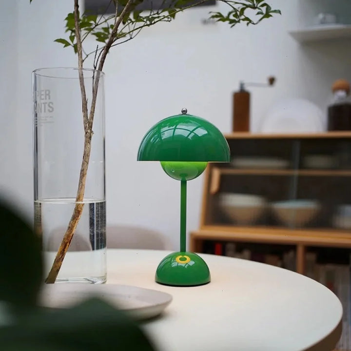 Groene tafellamp met halfronde kap op een ronde witte tafel, naast een glazen vaas met tak 43