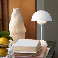 Witte mat uitgevoerde lamp op een tafel naast een ruwe beige vaas, boeken en citroenen 12