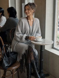 Model in grijze gebreide jurk zit in een café aan een marmeren tafeltje met koffie 4