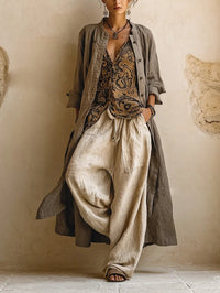Model draagt de complete set: lange taupe overjas open over gepatroneerde top en wijde beige broek, vooraanzicht 1