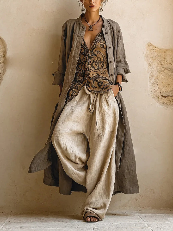 Model draagt de complete set: lange taupe overjas open over gepatroneerde top en wijde beige broek, vooraanzicht 1