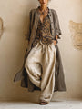 Model draagt de complete set: lange taupe overjas open over gepatroneerde top en wijde beige broek, vooraanzicht 1