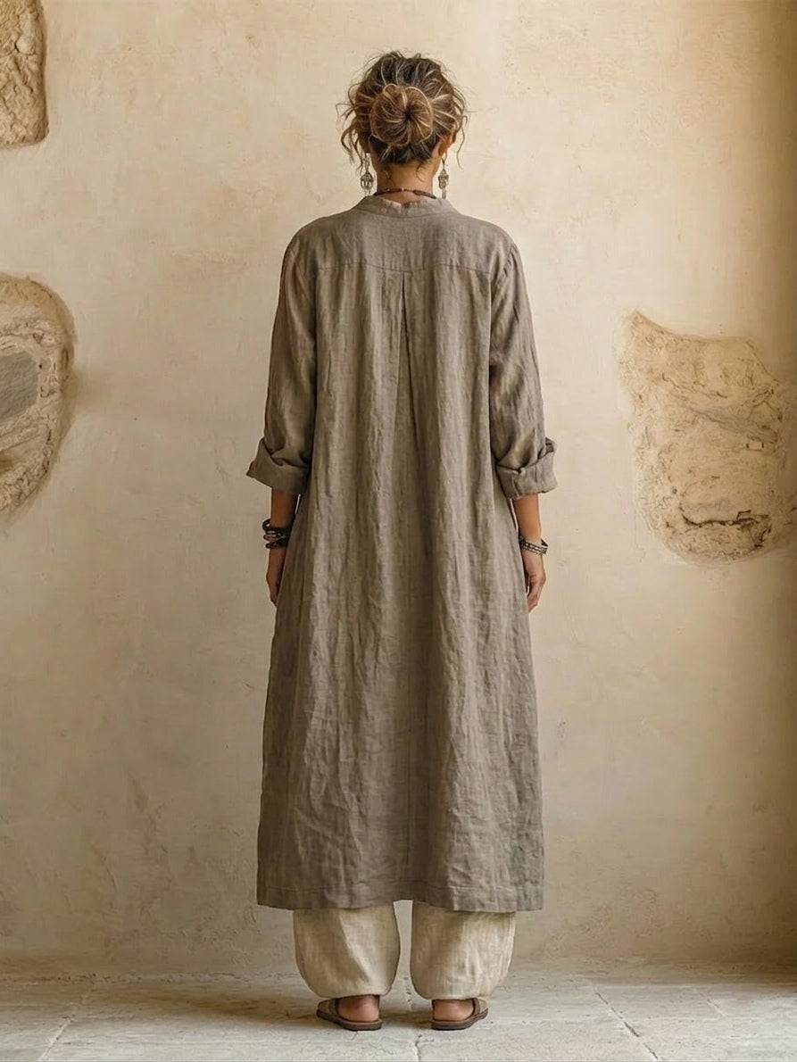 Achteraanzicht van de lange taupe overjas met opgerolde mouwen en een middenplooi, met wijde beige broek 5