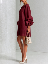 Zijaanzicht van bordeauxrode mini-jurk met pofmouw en roosmanchet, model met beige handtasje met bloemen en crèmekleurige pumps. 36