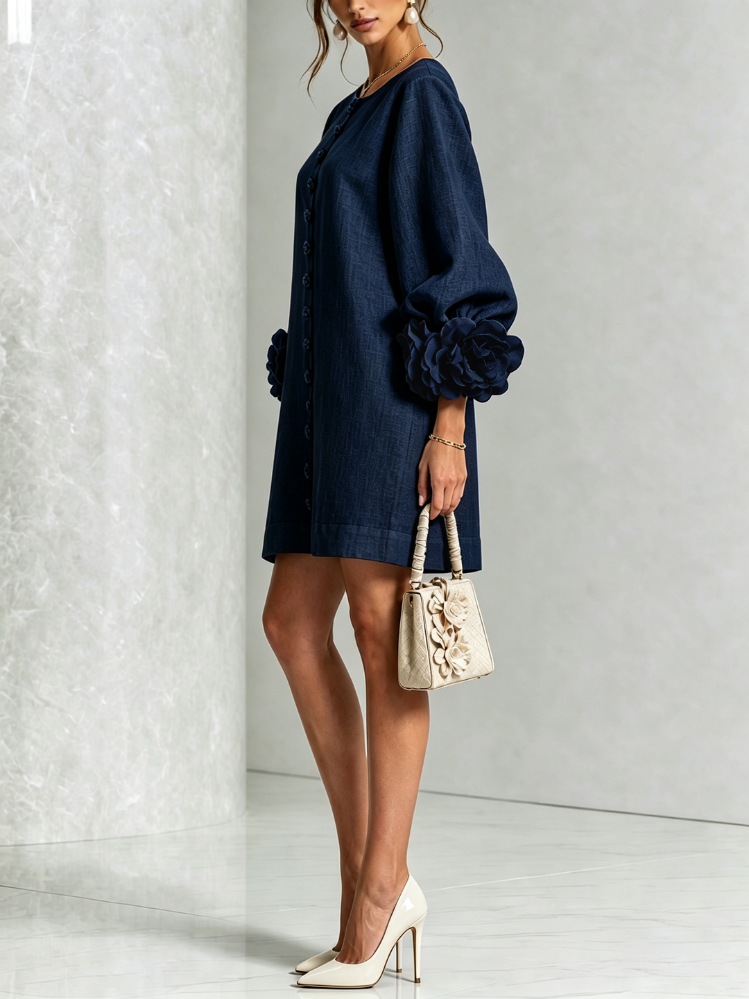Donkerblauwe jurk van opzij gefotografeerd op een model met beige handtas en lichte pumps, met roosmanchet op de pofmouw. 12