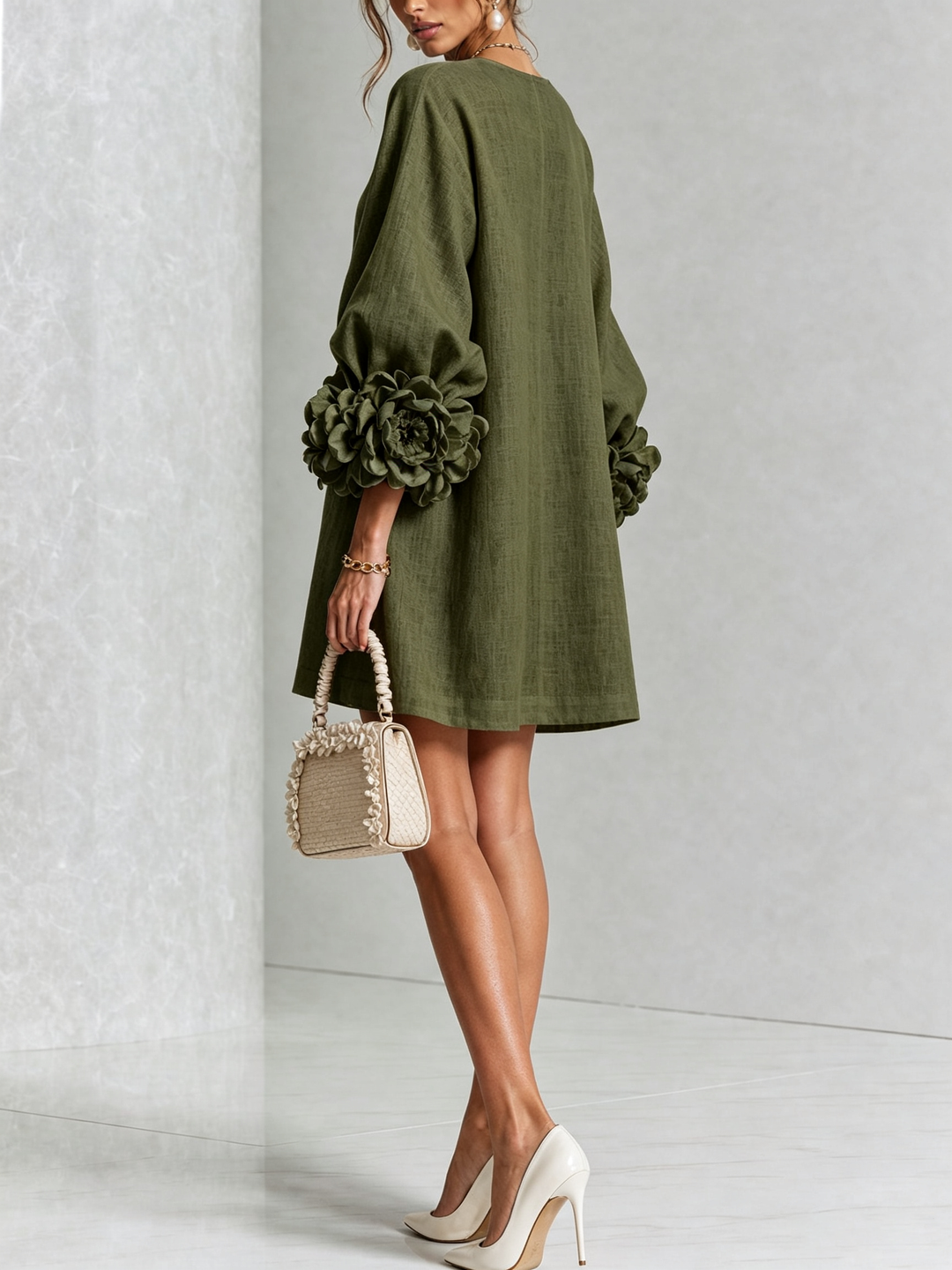 Model in de groene jurk van achteren en schuin opzij, met roosmanchetten en een beige handtas met ruches. 9