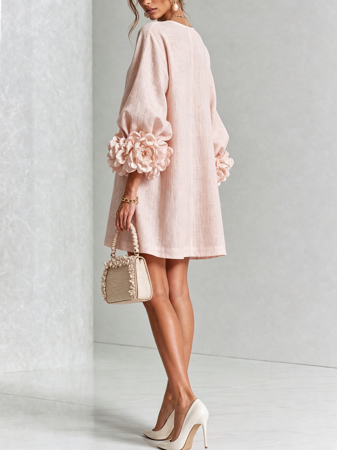 Model in roze mini-jurk, achterkant en zijaanzicht, met grote rozenmanchetten, beige handtasje en crèmekleurige pumps in een lichte studio. 21