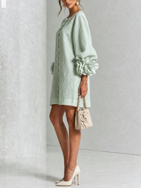 Zijaanzicht van lichtgroene mini-jurk met pofmouw en roosmanchet, model met beige handtasje en glanzende pumps. 32