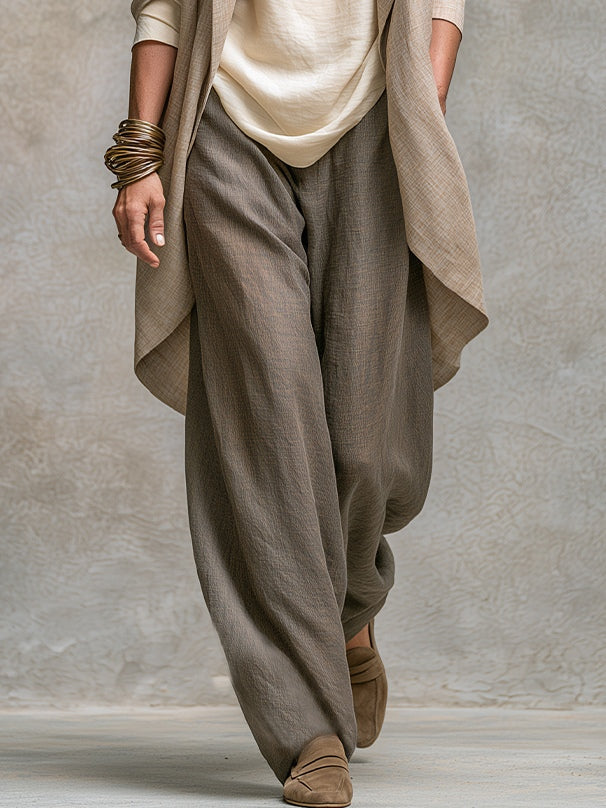 Detail van de taupe broek met wijde pijpen in lichte linnenstructuur, gedragen met suède loafers onder de open jack. 5