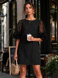Model draagt de zwarte jurk buiten voor een terras, met een koffiebeker in de ene en een beige tas in de andere hand. 4