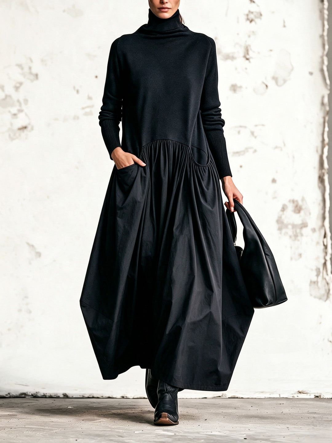 Model in zwarte maxi-jurk met col en geplooide rok, één hand in de zak, zwarte tas 1