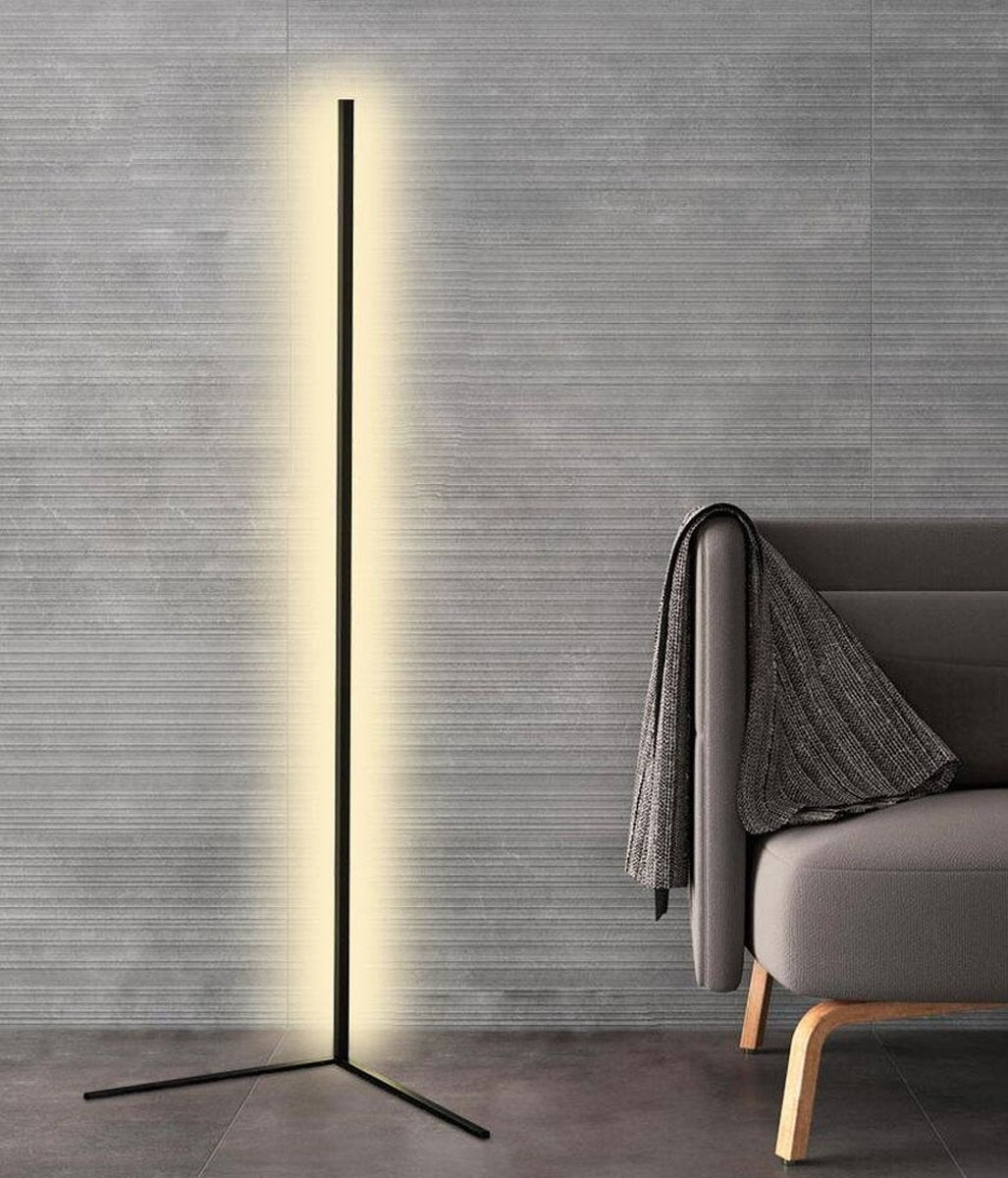 Hoge zwarte lamp met witte gloed tegen een grijze gestructureerde muur naast een bank met omgeslagen deken 8