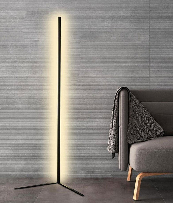 Hoge zwarte lamp met witte gloed tegen een grijze gestructureerde muur naast een bank met omgeslagen deken 8