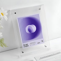 Helder transparante acryl lijst met een paarse abstracte print van een cirkel en verticale lijnen, naast witte bloemen. 16