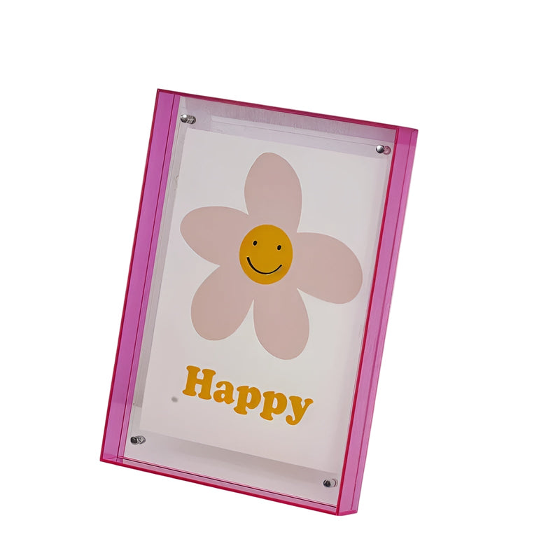 Roze acryl fotolijst met transparante voorkant, schuin opgesteld, met een illustratie van een bloem met lachend gezichtje erin. 1