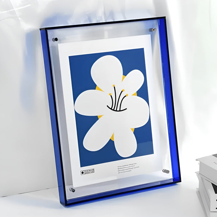 Blauwe acryl lijst met een illustratie van een grote witte bloem op blauwe achtergrond, tegen een lichte muur. 14