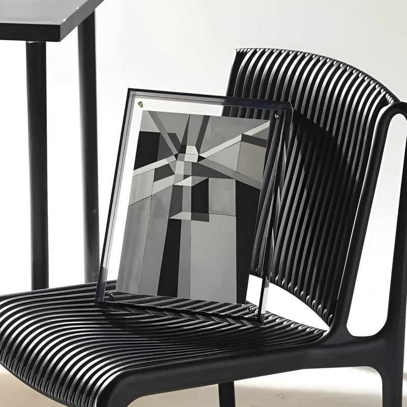 Zwart-wit geometrische print in een acryl lijst met donkere rand, schuin tegen een zwarte stoel geplaatst. 7