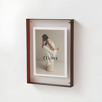 Rode acryl lijst met zwarte rand aan de muur, met een foto van een gehurkte vrouw in een wit jurkje. 20
