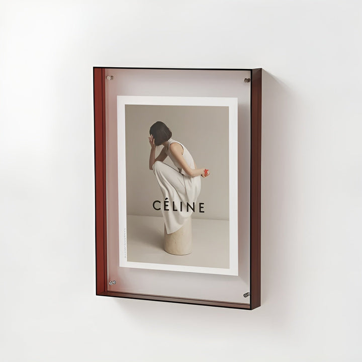 Rode acryl lijst met zwarte rand aan de muur, met een foto van een gehurkte vrouw in een wit jurkje. 20