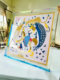 Grote transparante acryl lijst met blauwe onderrand, vastgehouden met één hand, met een sjaal vol dieren en vlinders erin. 17