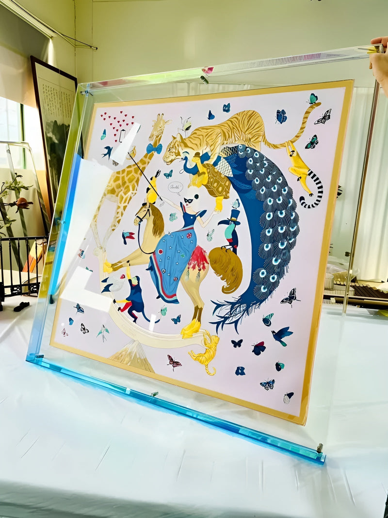 Grote transparante acryl lijst met blauwe onderrand, vastgehouden met één hand, met een sjaal vol dieren en vlinders erin. 17