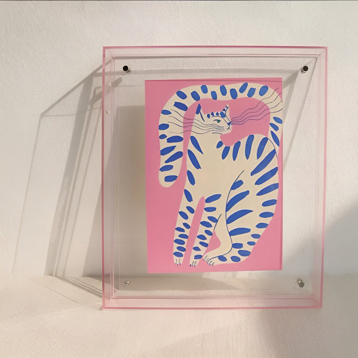 Transparante acryl lijst met roze randje en een roze print van een witte kat met blauwe strepen. 9
