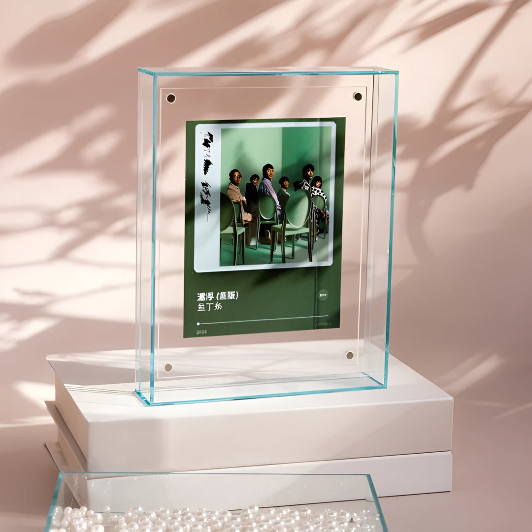 Doorzichtige acryl lijst met lichtgroene rand op een witte stapel, met een groene albumhoes-achtige print, tegen een roze achtergrond. 13