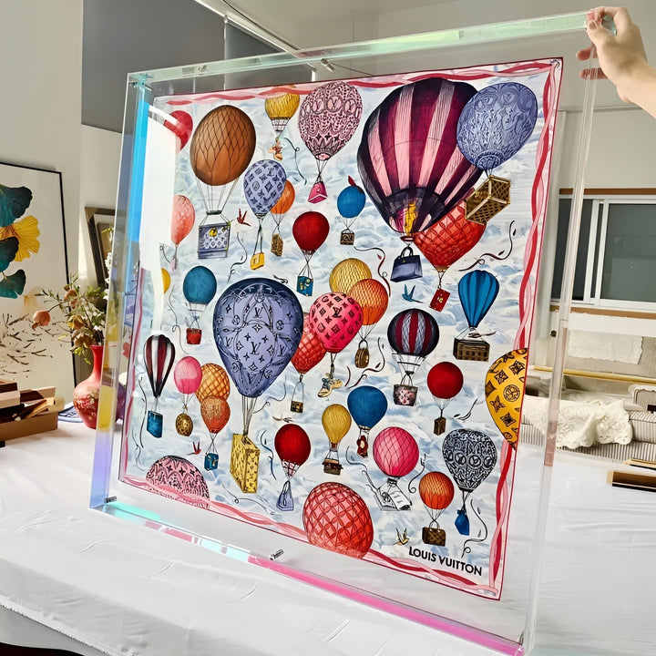 Grote transparante acryl lijst met regenboogschitterende rand, vastgehouden met één hand, met een sjaal met luchtballonnen erin. 11