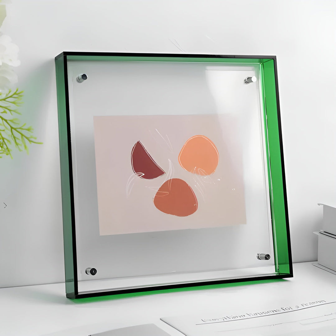 Doorzichtige acryl fotolijst met groene rand en zichtbare bevestigingsschroefjes, staand op een witte tafel met een abstract kunstwerk erin. 21
