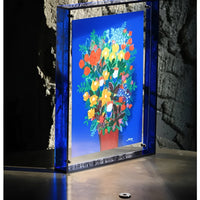 Staande blauwe acryl lijst met een kleurrijk bloemenboeket erin, geplaatst voor een ruwe stenen muur. 4