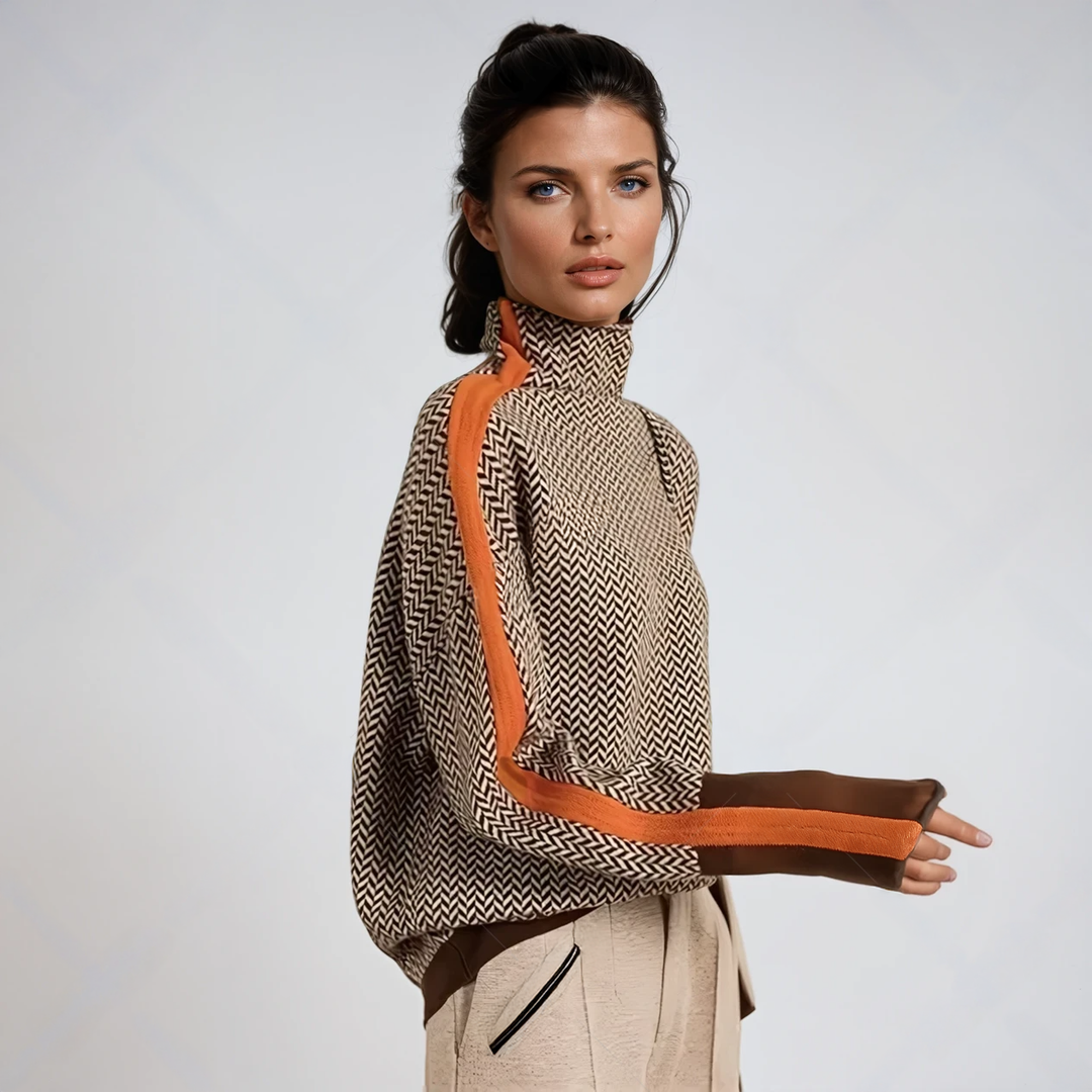 Model in zijaanzicht draagt de trui met visgraatpatroon, oranje streep langs de mouw en bruine manchetten, met een beige broek. 1