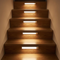 Vijf lichtbalken op de stootborden van een houten trap, die elke trede in warm licht zetten. 2